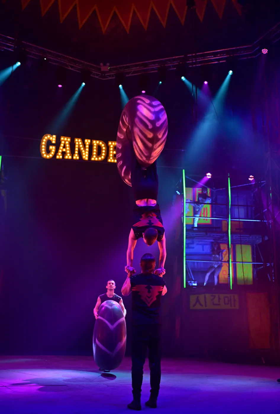 Acrobats balance a tower of performers and a giant inflatable ring beneath the Gandeys sign