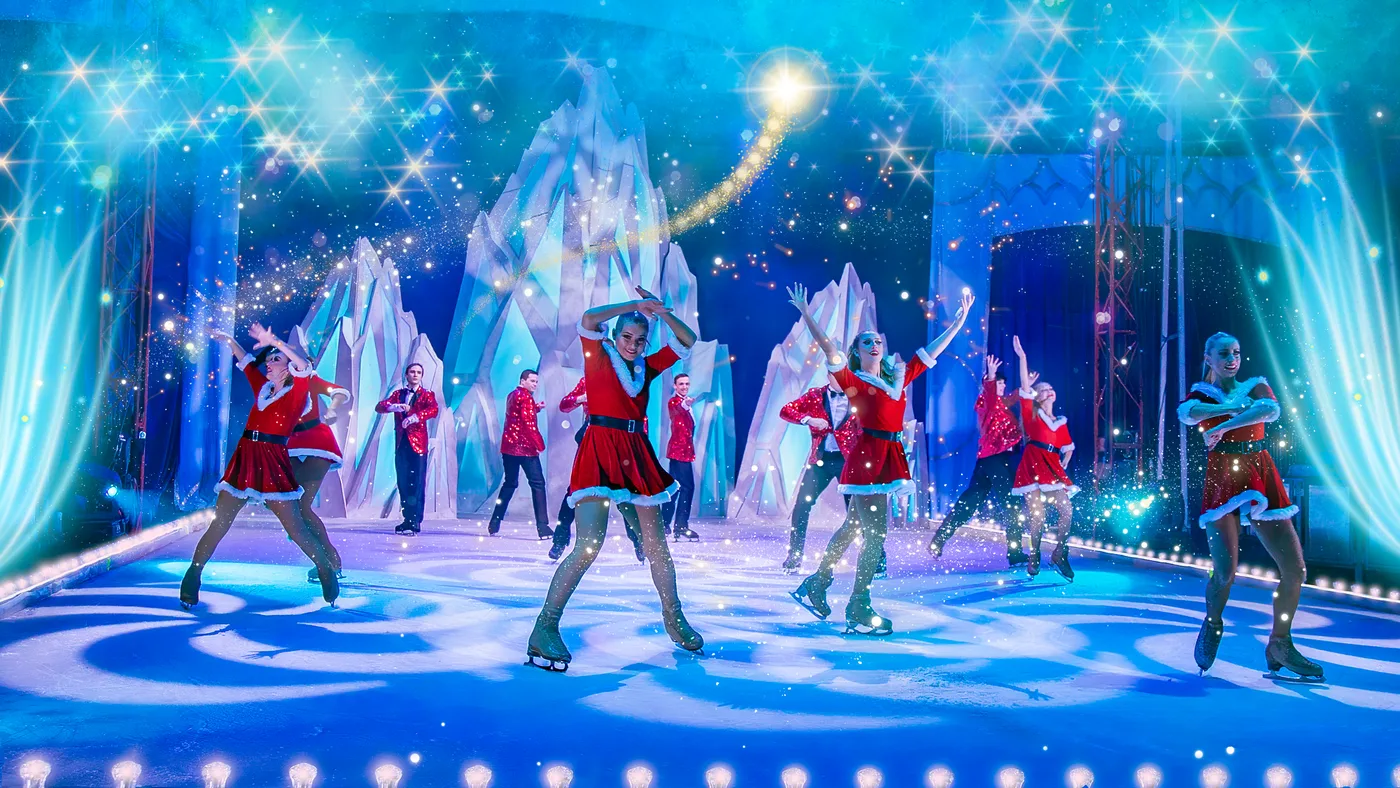 Skaters in red coats on a blue-lit rink in front of an ice castle set