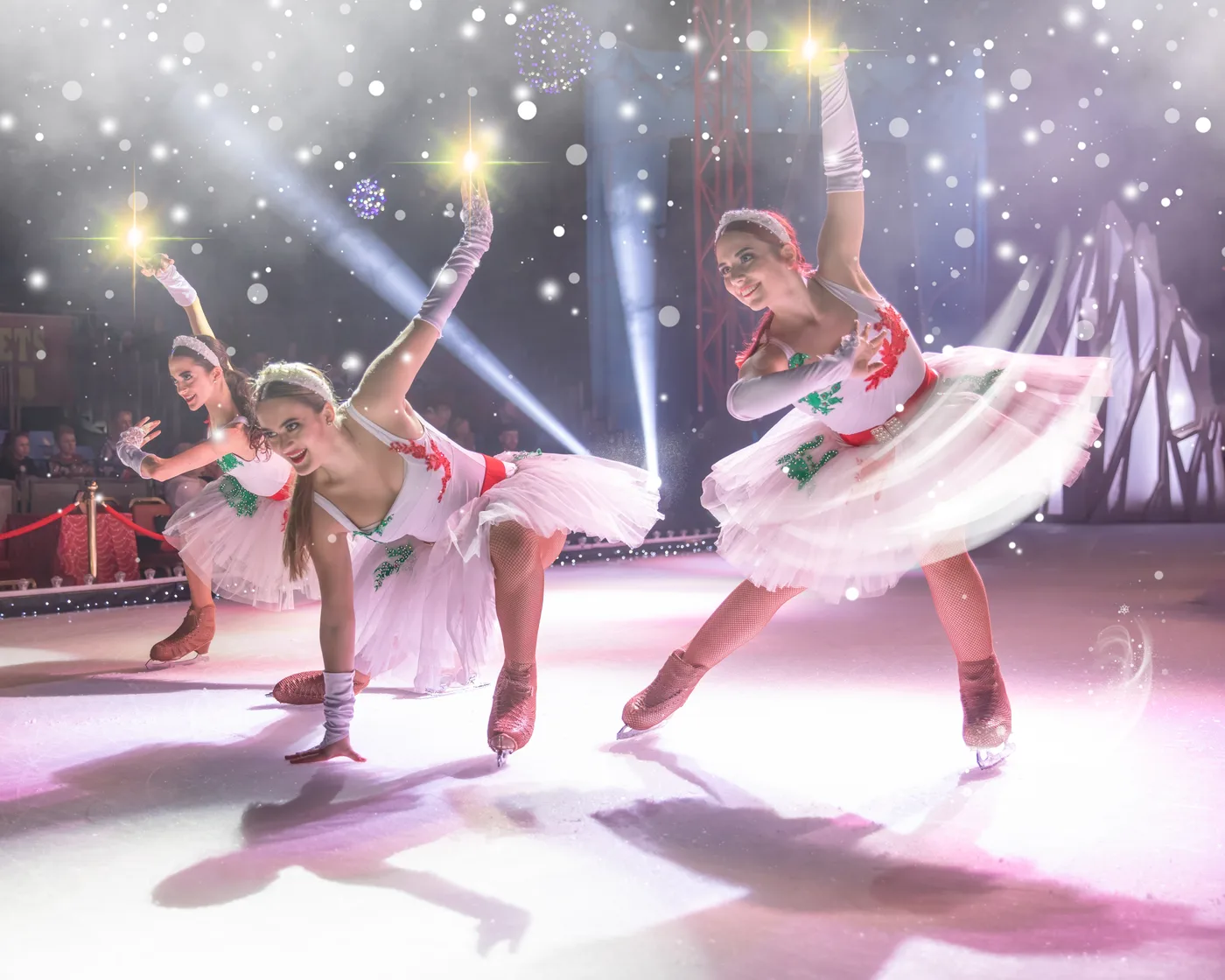 Three skaters in white tutus with red flowers bow low on the ice