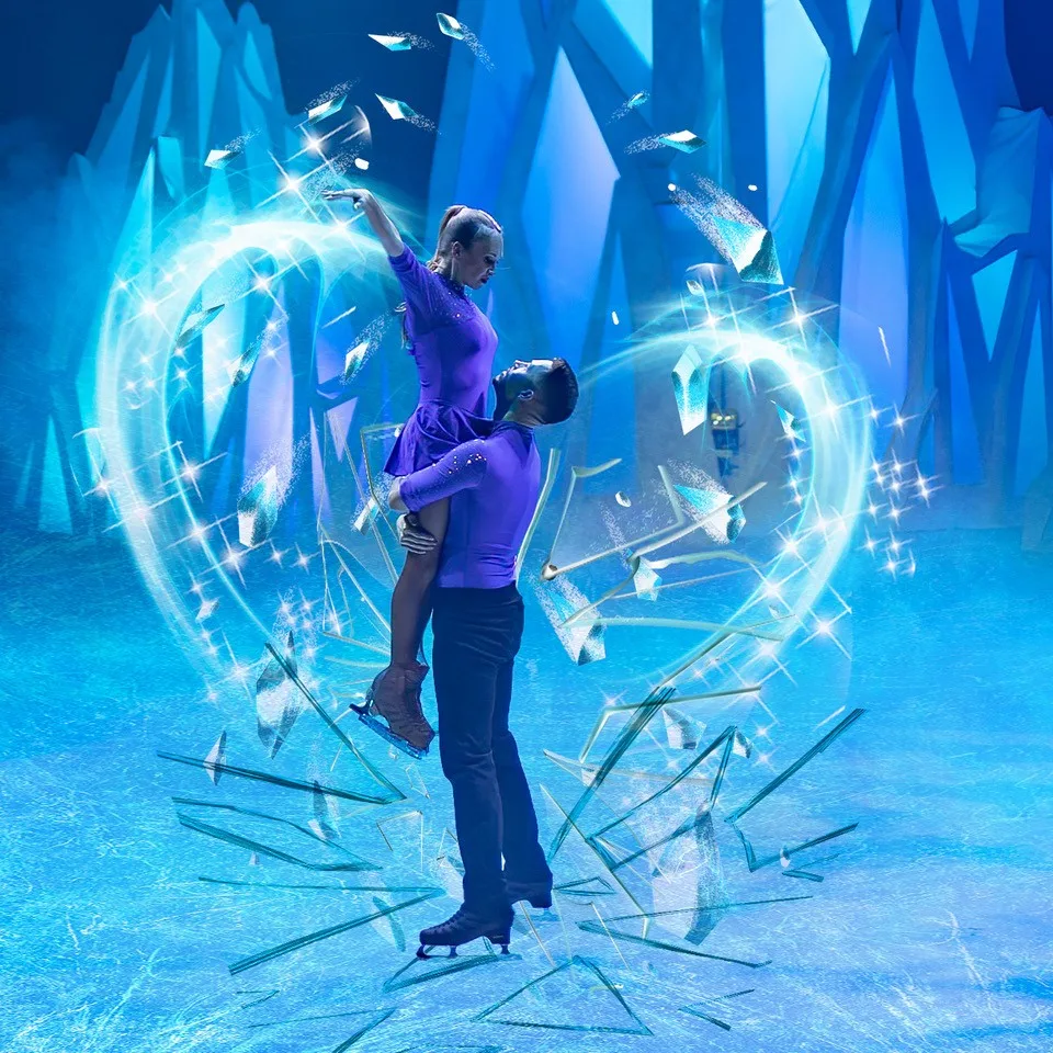 A skater lifts his partner in a purple dress inside a heart shape of ice shards